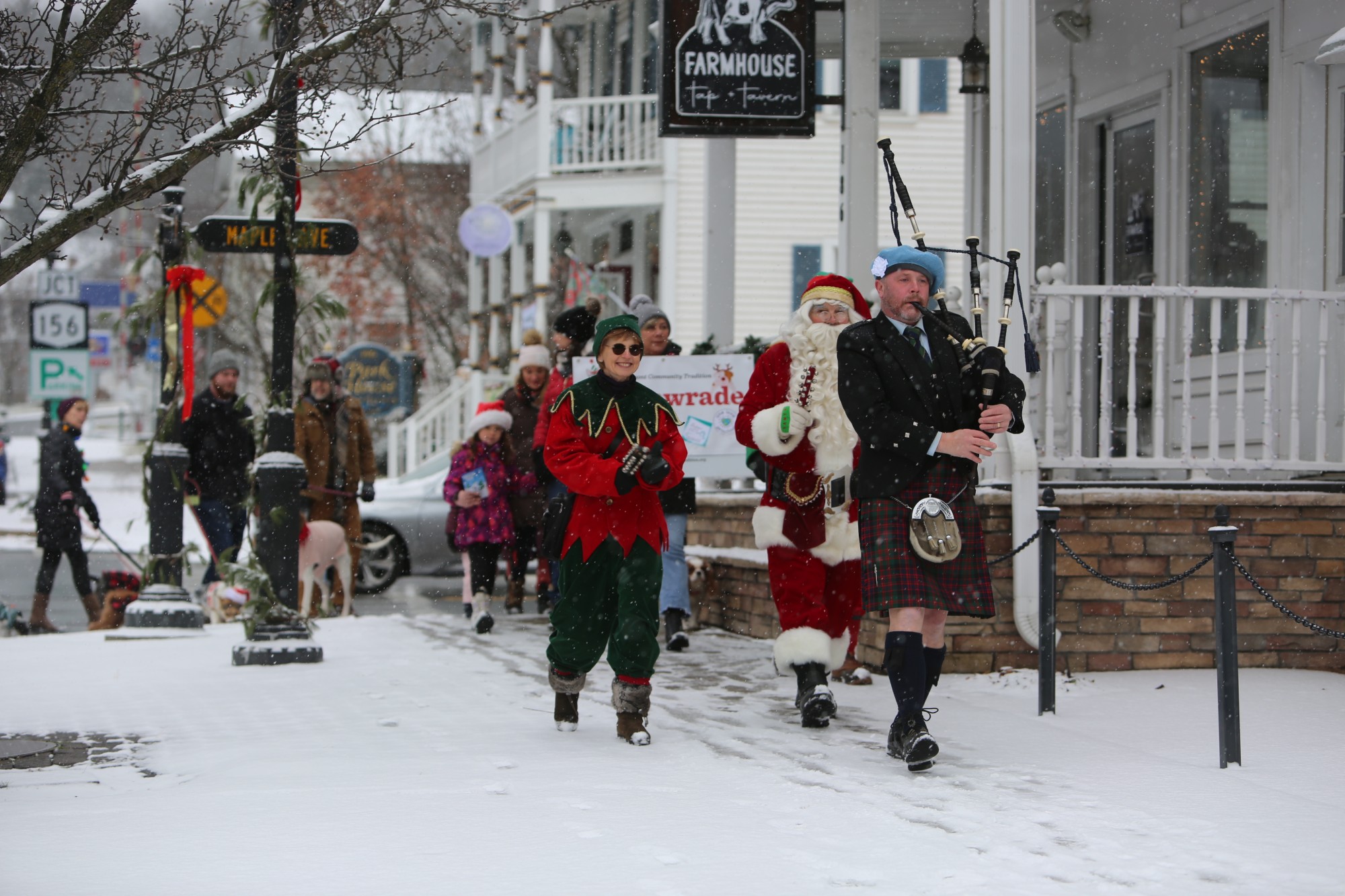 A bagpiper, Santa, and an elf lead a snowy holiday parade past the Farmhouse Tap + Tavern