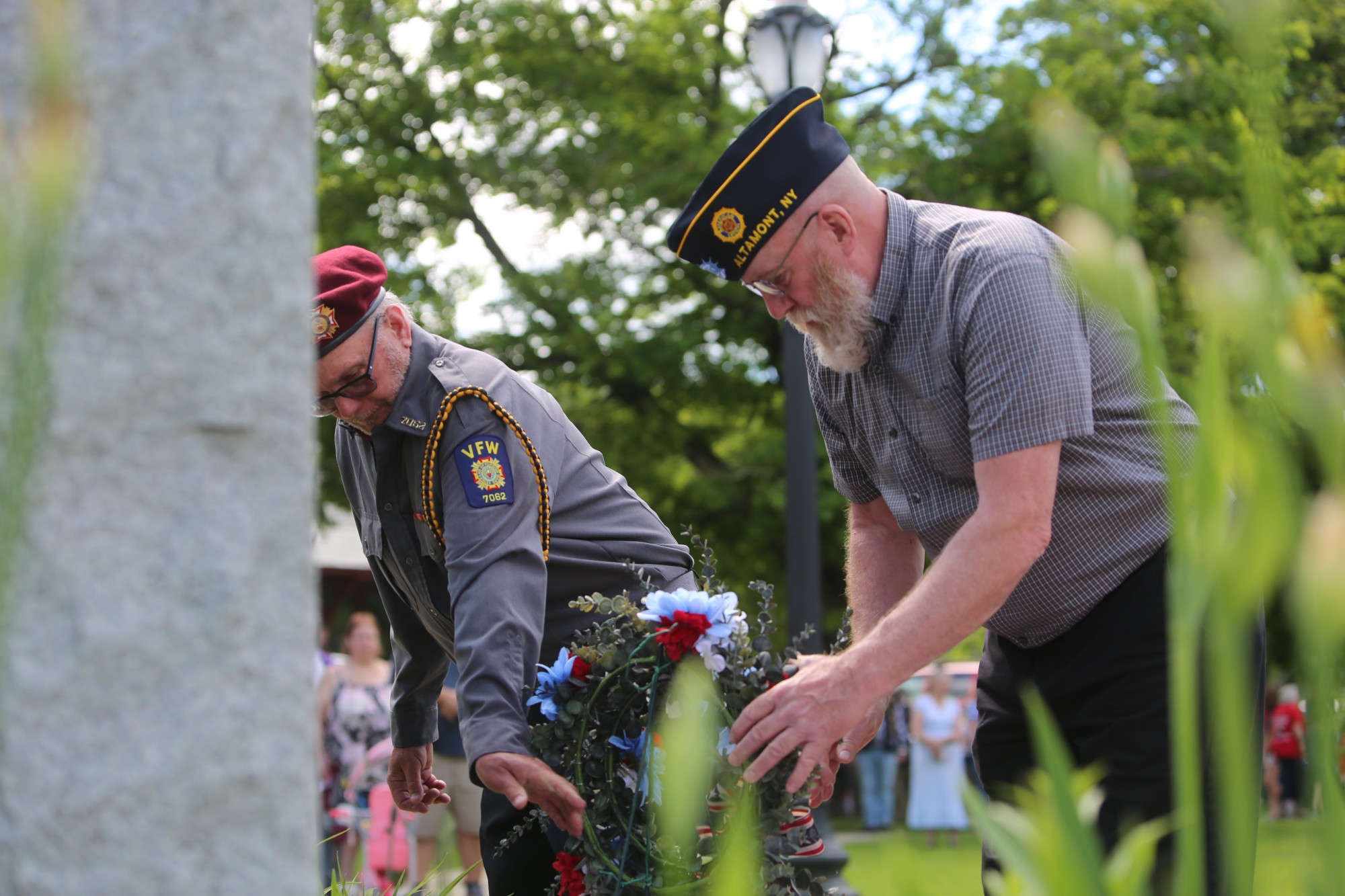 Two veterans place a memorial wreath at a stone monument