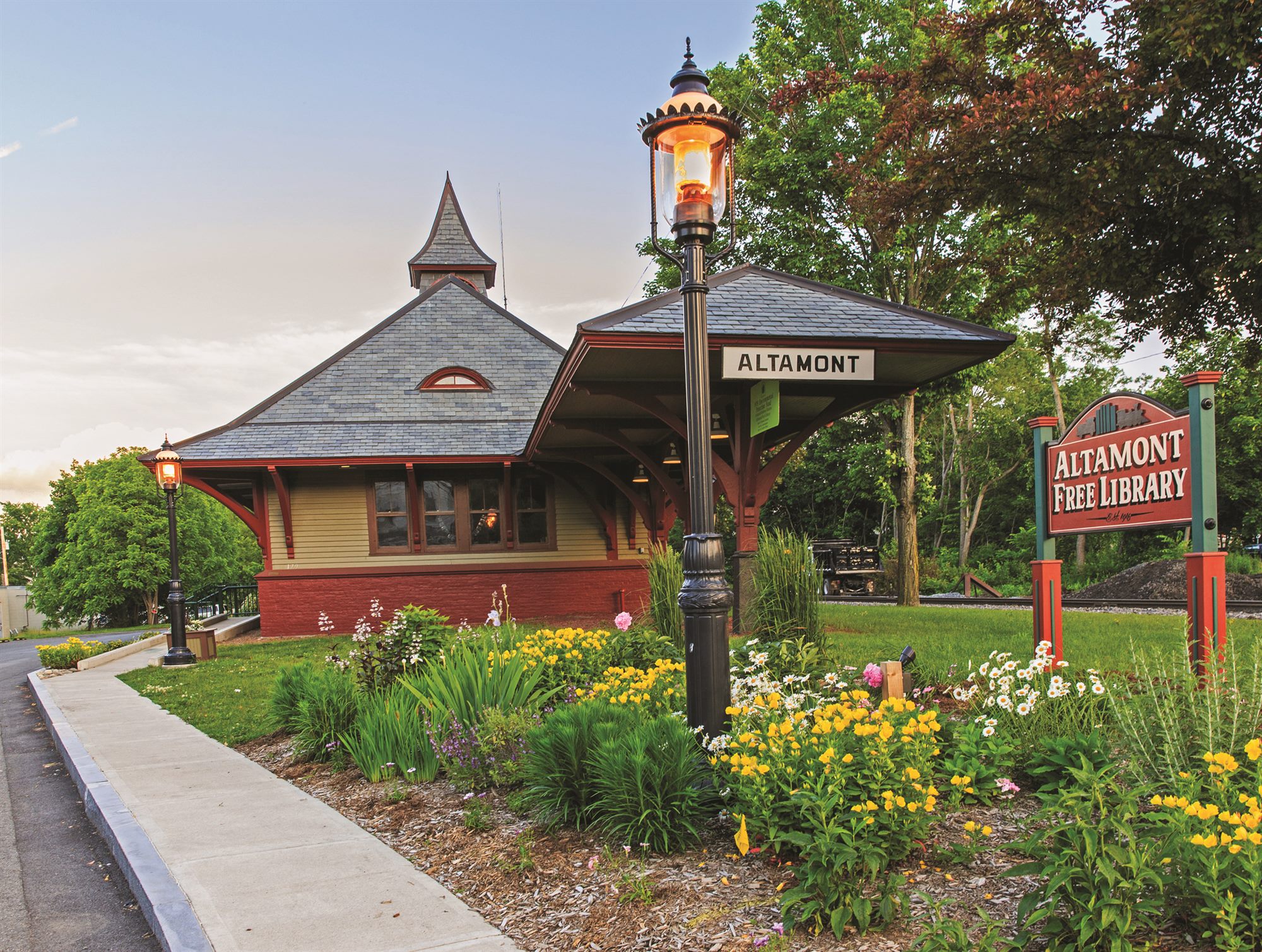 The Altamont Free Library in the village's old train depot, with a gas lamp and summer flower beds